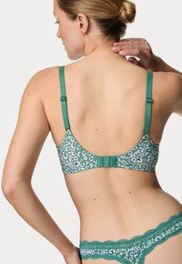 Zelená podprsenka s leopardím potiskem, s nastavitelnými ramínky a háčkovým zapínáním. Měkká tkanina s texturovaným krajkovým lemováním podél okrajů.