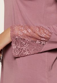 Vêtement à manches longues mauve avec un accent de bordure en dentelle aux poignets, présentant des motifs floraux et un tissu lisse et léger.