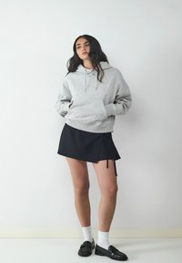 Szary bawełniany hoodie z sznurkiem, w połączeniu z czarną mini spódniczką z bocznym wiązaniem. Uzupełniony białymi skarpetkami i czarnymi loafersami.