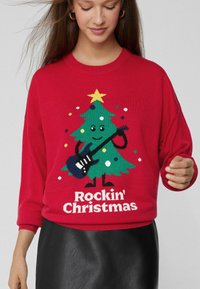 Roter Strickpullover mit einer Grafik eines Weihnachtsbaums, der eine Gitarre hält, bunten Ornamenten und dem weißen Schriftzug "Rockin' Christmas".