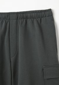 Pantaloni della tuta grigio scuro con cintura elastica, tasca laterale e texture liscia e morbida. Design casual con dettagli minimalisti.