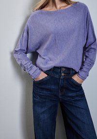 Löst sittande, mjuk lavendelfärgad tröja med skräddarsydda ärmar, kombinerad med högmidjade, mörkblå denimjeans med tvåknappsstängning.