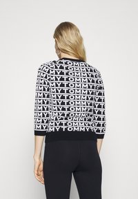 Schwarz-weißer Strickpullover mit wiederholtem "TOMMY"-Textmuster, 3/4-Ärmeln und geripptem Saum am Halsausschnitt und dem unteren Rand.