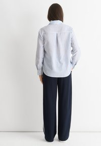 Blue and white striped blouse with long sleeves, buttoned cuffs, and a back yoke detail, paired with high-waisted navy wide-leg trousers.
