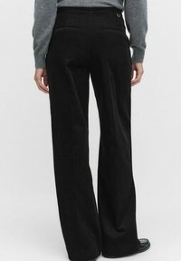 Zwarte corduroy wijde pijpen broek met een textuurafwerking, voorzien van twee achterzakken en een hoge taille.