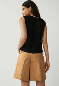 Haut sans manches en tricot noir avec un design en dentelle délicat et des bords en scallop, associé à un short beige ajusté. Texture douce et coupe décontractée.