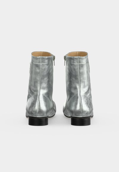 Paire de bottines métalliques argentées avec des talons bas noirs, vues de dos sur fond blanc.