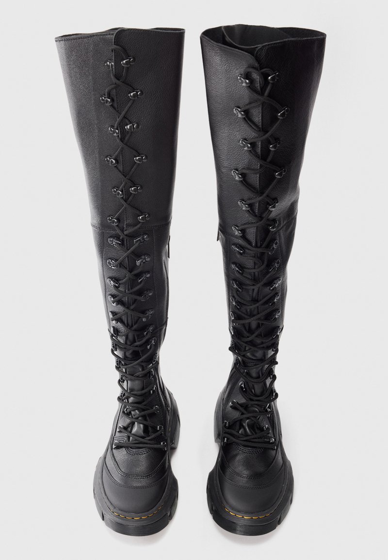 Un paio di stivali in pelle neri al ginocchio con suole spesse e lacci frontali su uno sfondo semplice.