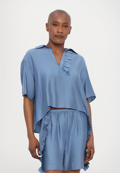Light blue two-piece outfit features a short-sleeve, collared top with ruffle accents and matching shorts with ruffled edges. Smooth texture.