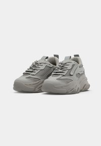 Grey athletic sneakers with mesh and textured details, chunky rubber sole, contrasting laces, and rear pull tab for easy wear.