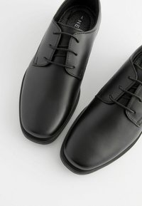 Chaussures habillées en cuir noir avec bout arrondi, finition lisse et design à laçage avec quatre œillets. Semelles intérieures texturées avec un motif géométrique.