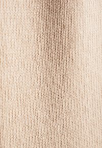 Lichtbeige gebreide stof met een zachte textuur, met een consistent patroon en subtiele variaties in draaddiktes.