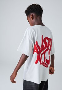 Hvid bomulds-t-shirt med fremtr�ædende rød grafisk tekst på ryggen. Kortærmet, rummelig pasform og rund hals.