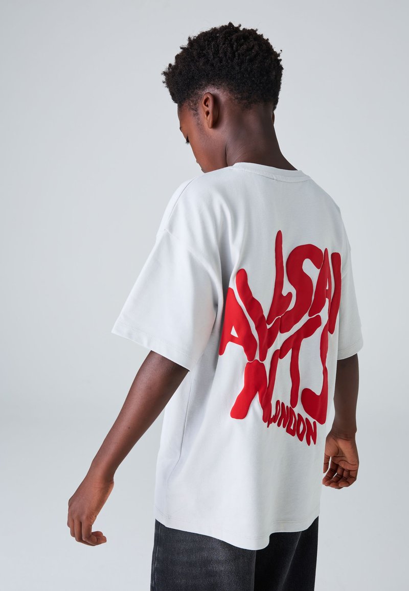 Hvid bomulds-t-shirt med fremtrædende rød grafisk tekst på ryggen. Kortærmet, rummelig pasform og rund hals.