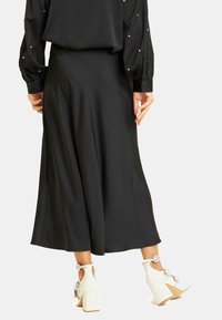 Falda midi negra con un diseño fluido y una textura suave, combinada con botas de tobillo blancas con tacones gruesos y acentos decorativos.