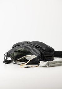 Borsa in pelle nera con la zip aperta, che rivela un interno verde chiaro. Presenta spallacci regolabili e una borsa grigia aggiuntiva.