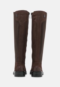 Brązowe skórzane kozaki do kolan z bocznymi zapięciami, teksturowanymi panelami, gumowymi podeszwami i małą metką z logo w pobliżu pięty.