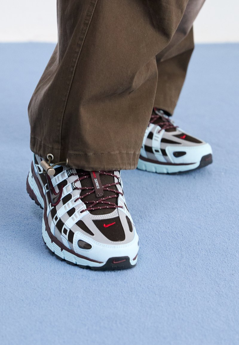 Baskets Nike avec une combinaison de couleurs bleu clair et marron, en matériau mesh et caoutchouc, avec des accents rouges contrastés et une semelle texturée.