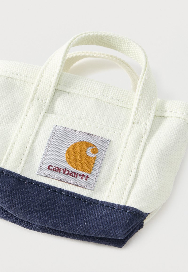 Piccola borsa a tracolla in tela bianca e blu navy con due manici e una toppa con il logo Carhartt sul davanti.