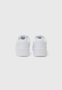 Białe sneakersy z gładkiej skóry na zewnątrz, o zaokrąglonym czubku i wyściełanym kołnierzu. Posiadają grubą podeszwę oraz minimalne perforacje dla lepszej wentylacji.