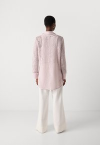 Roze opengewerkt lange mouwen shirt met een kraag, voorzien van een patroonstructuur, gecombineerd met witte wijde broekspijpen die een ontspannen silhouet tonen.