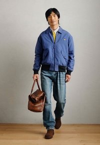 Μπλε μπουφάν τύπου bomber με δύο μπροστινές τσέπες, μαύρους ελαστικούς μανικιών, συνδυασμένο με ανοιχτό μπλε τζιν. Καφέ δερμάτινη τσάντα και καφέ μπότες.