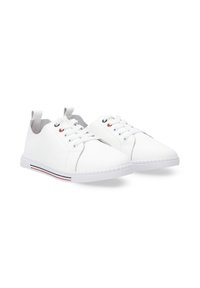 Białe sneakersy z gładką skórzaną cholewką, okrągłym noskiem, sznurowanym zapięciem i gumową podeszwą z czerwonymi i niebieskimi paskami po bokach.