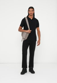 Sort polo skjorte, mørke lige bukser og sorte sneakers. Lysegrå crossbody taske med en glat overflade og lynlåslomme foran.