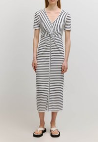 Gestreepte jurk in wit en marineblauw, met een V-hals, korte mouwen, een geknoopt middel en knopen aan de voorkant. Draag het met witte sandalen.