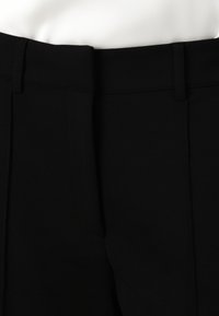 Pantalon noir tailleur avec une texture lisse, présentant un devant plat, des passants pour ceinture et des détails subtils de couture. Pas de poches visibles.