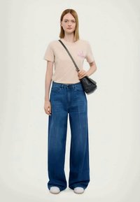 Ροζ μπλουζάκι με λουλουδάτο σχέδιο, σε συνδυασμό με φαρδιά τζιν παντελόνια. Η μαύρη τσάντα χιαστί και τα λευκά αθλητικά συμπληρώνουν την εμφάνιση.