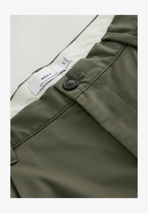 Olivengrønne bukser med smal pasform, sort knap og synligt hvidt indvendigt mærke med teksten "NEXT Regular Tapered Fit 32R."