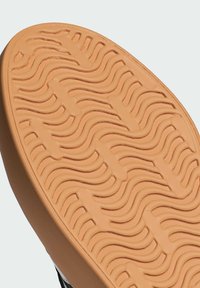 Gumeni potplat cipele u boji tan, s valovitom teksturom za bolju prionljivost, okružen tamnom gornjom ivicom.