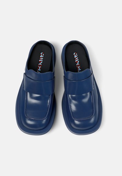 Navy blue leather slip-on shoes with a wide strap across the upper, cushioned sole, and textured lining. Smooth finish, square toe design.