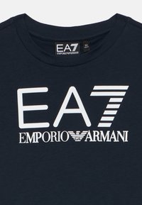 Tumesinine puuvillane t-särk, millel on valge graafiline trükk tekstiga "EA7" ja "EMPORIO ARMANI", ümara kaelusega ja pehme tekstuuriga.