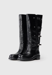 Bottes noires en cuir, montantes jusqu'au genou, avec une texture lisse, dotées de trois sangles à boucle sur le côté et d'un design de talon bas.