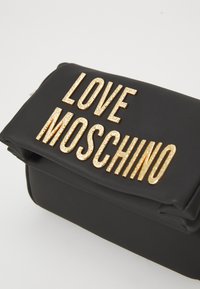Black leather clutch bag with large textured gold letters spelling "LOVE MOSCHINO" on the flap.