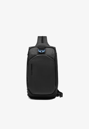 Sac à dos bandoulière noir avec un panneau avant texturé, des accents lisses, une fermeture éclair supérieure et une attache bleue. Conception compacte et durable avec sangle réglable.