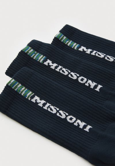 Tre par mørkeblå ribbestrikkede sokker med hvite "MISSONI"-logoer og grønne, blå og hvite striper nær mansjettene.