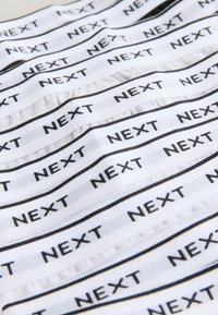 Bijela tkanina s ponavljajući crnim natpisom "NEXT," koja ima mekanu teksturu i glatku završnicu, prikazana u uzorku vala.