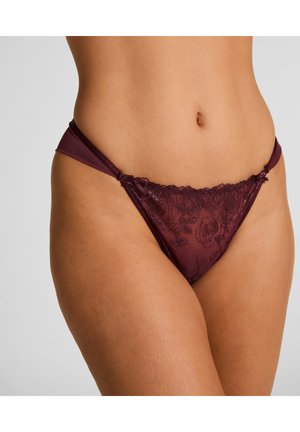 String en dentelle bordeaux avec motif floral, présentant des bretelles réglables et une texture semi-transparente. Couverture minimale avec des détails délicats.