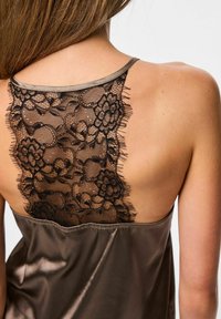 Top marrone in satin con schiena in pizzo nero trasparente decorato con motivi floreali e bordi sfilacciati, spalline sottili e una texture morbida e lucida.