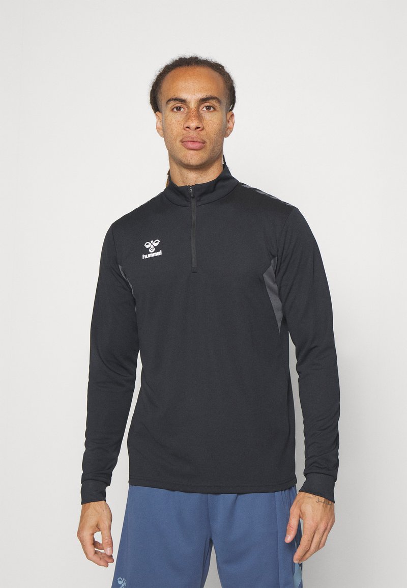 Top sportivo zip-up nero con maniche lunghe, presenta dettagli grigi sui lati e un logo sul petto. Texture liscia e design aderente.