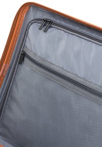 Interior de una bolsa de viaje marrón con tejido gris, que presenta un bolsillo con cremallera y una sección con textura de panal. Se pueden ver dos tiradores de cremallera.