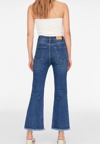 Jean évasé taille haute en denim bleu foncé avec un ourlet effiloché, doté de poches arrière classiques et d'une étiquette à la taille.