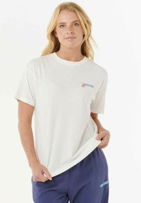 Weißes Baumwoll-T-Shirt mit Rundhalsausschnitt, kurzen Ärmeln und einem bunten Logo auf der Brust. Getragen mit marineblauen Hosen, die hellblaumen Text haben.