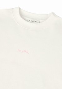 Felpa bianca realizzata in tessuto morbido, con scollatura rotonda e un piccolo logo ricamato in rosa che recita "OH APRIL."