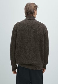 Brązowy, teksturowany sweter z dzianiny z wysokim kołnierzem i luźnym krojem. Posiada opadające ramiona i ściągacze przy mankietach. Wyświetlony widok z tyłu.