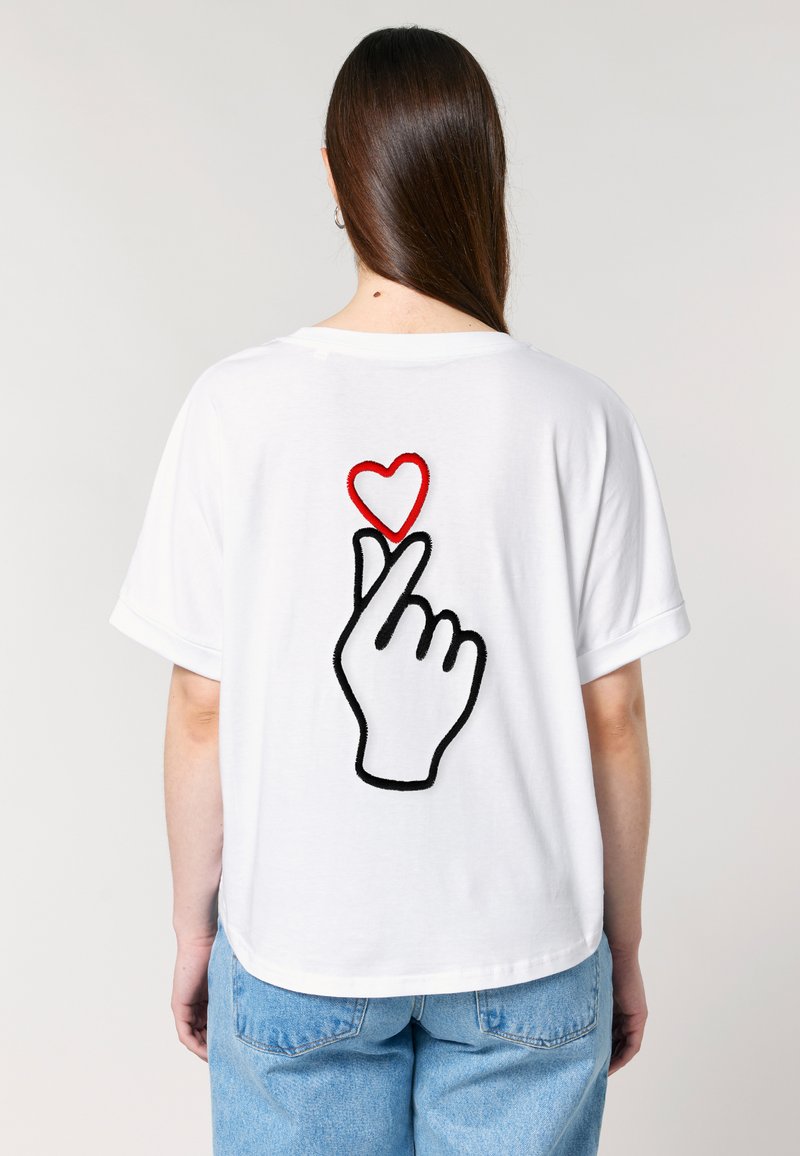 Witte t-shirt met korte mouwen en een grote geborduurde afbeelding op de achterkant van een hand en een rood hart. Casual pasvorm.