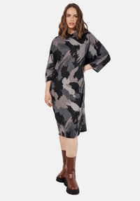 Langere mouw jurk in zwart, grijs en witte abstracte patronen, gemaakt van zachte stof. Gecombineerd met bruine heeled boots met chunky zolen.